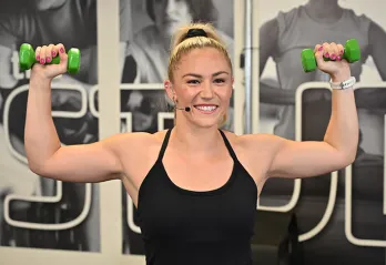 Exercise instructor smiling and flexing muscles while holding weight.s
